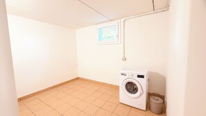 Un cuarto de lavandería con lavadora, una ventana pequeña y suelo de baldosas.
