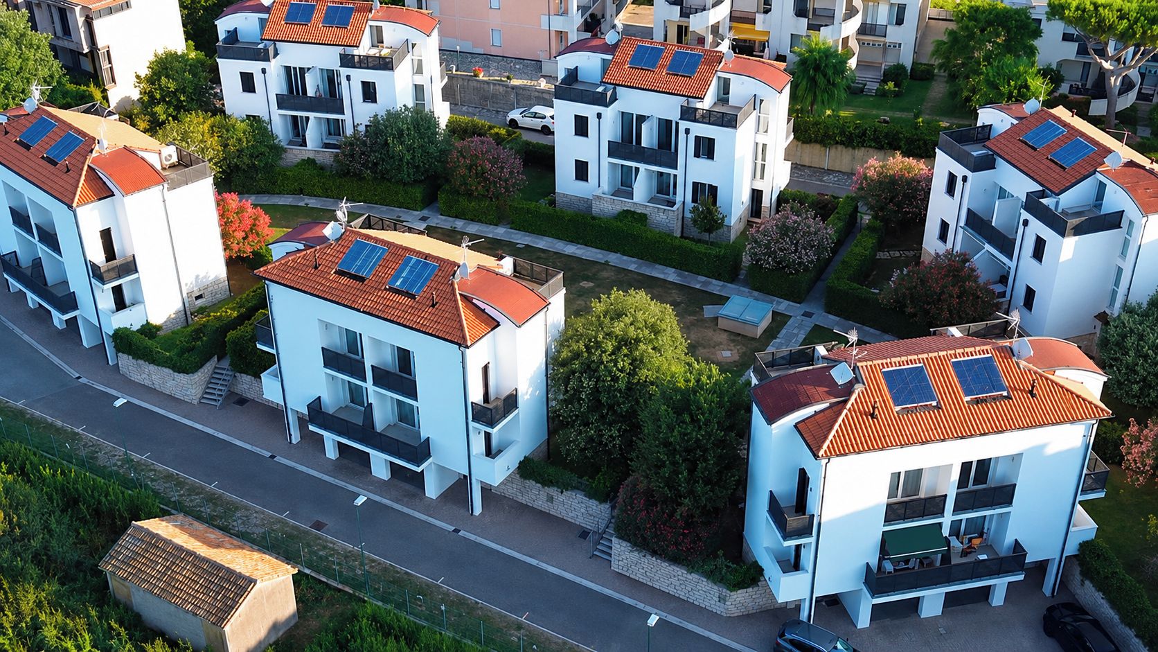 Zona residencial amb edificis blancs moderns, panells solars als terrats i una carretera ben cuidada.