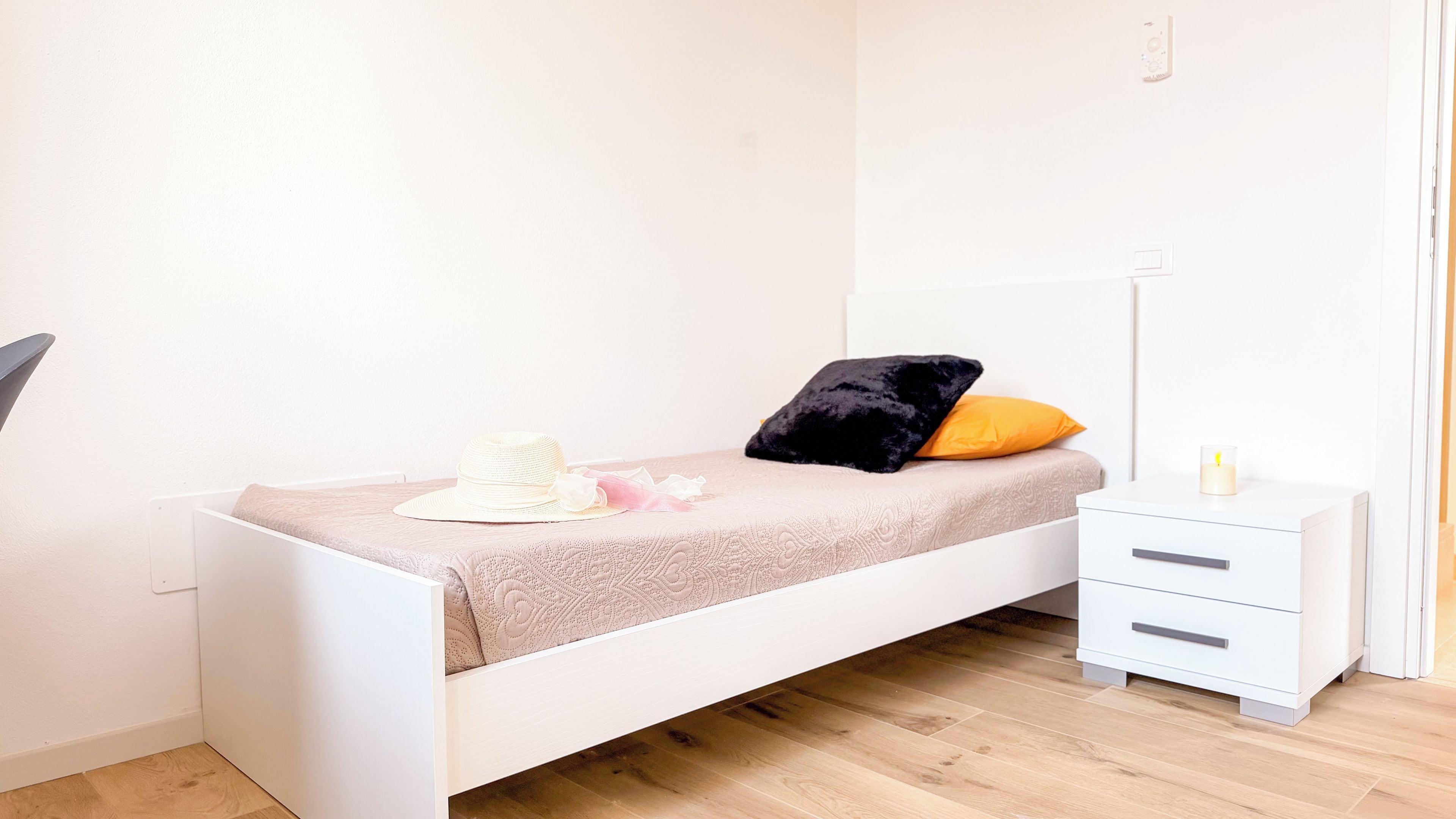 A single bed with a white frame, a bedside table with drawers, and a nightstand with a lamp.