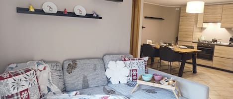 A living room with a sofa, a dining table, and a kitchen area with a stove and cabinets.