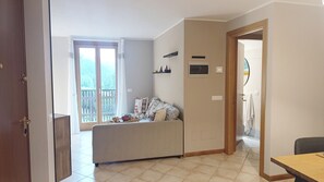 A living room with a sofa, a dining table, and a balcony with a view. - La Casa di Fede By Ca-sa Check (Aprica)