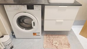 A front-loading washing machine with a control panel, a white cabinet with drawers, and a floral-patterned mat on the floor. - La Casa di Fede By Ca-sa Check (Aprica)