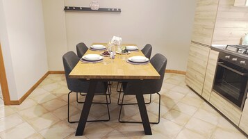 Uma sala de jantar com uma mesa de madeira posta para seis, cadeiras pretas e uma cozinha com forno moderno.