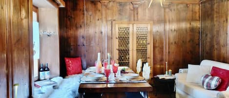 A wooden interior with a dining table set for four, a white sofa, and a red pillow.