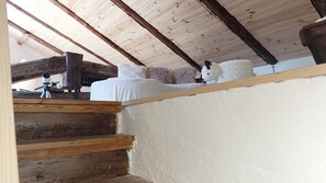 Escada de madeira que leva a um quarto com parede branca e um objeto branco e fofo sobre uma prateleira de madeira.