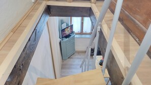 Um quarto em estilo loft com piso de madeira, uma televisão em um móvel e uma janela com cortinas.