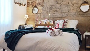 Ein ordentlich bezogenes Bett mit einer grünen Decke, ein kleiner Tisch mit einer Lampe und Zierkissen.