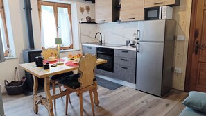 Cozinha compacta com geladeira, fogão e micro-ondas. Há uma mesa de jantar com cadeiras e uma janela com cortinas.