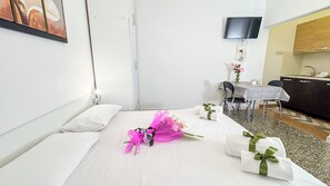 A hotel room with a bed, a desk, a chair, a TV mounted on the wall, and a small kitchenette. - Cà 4 Nevodi Jennifer by Ca-Sa Check - MS 2 NTCà 4 Nevodi Jennifer by Ca-Sa Check - MS 2 NT (Chioggia)