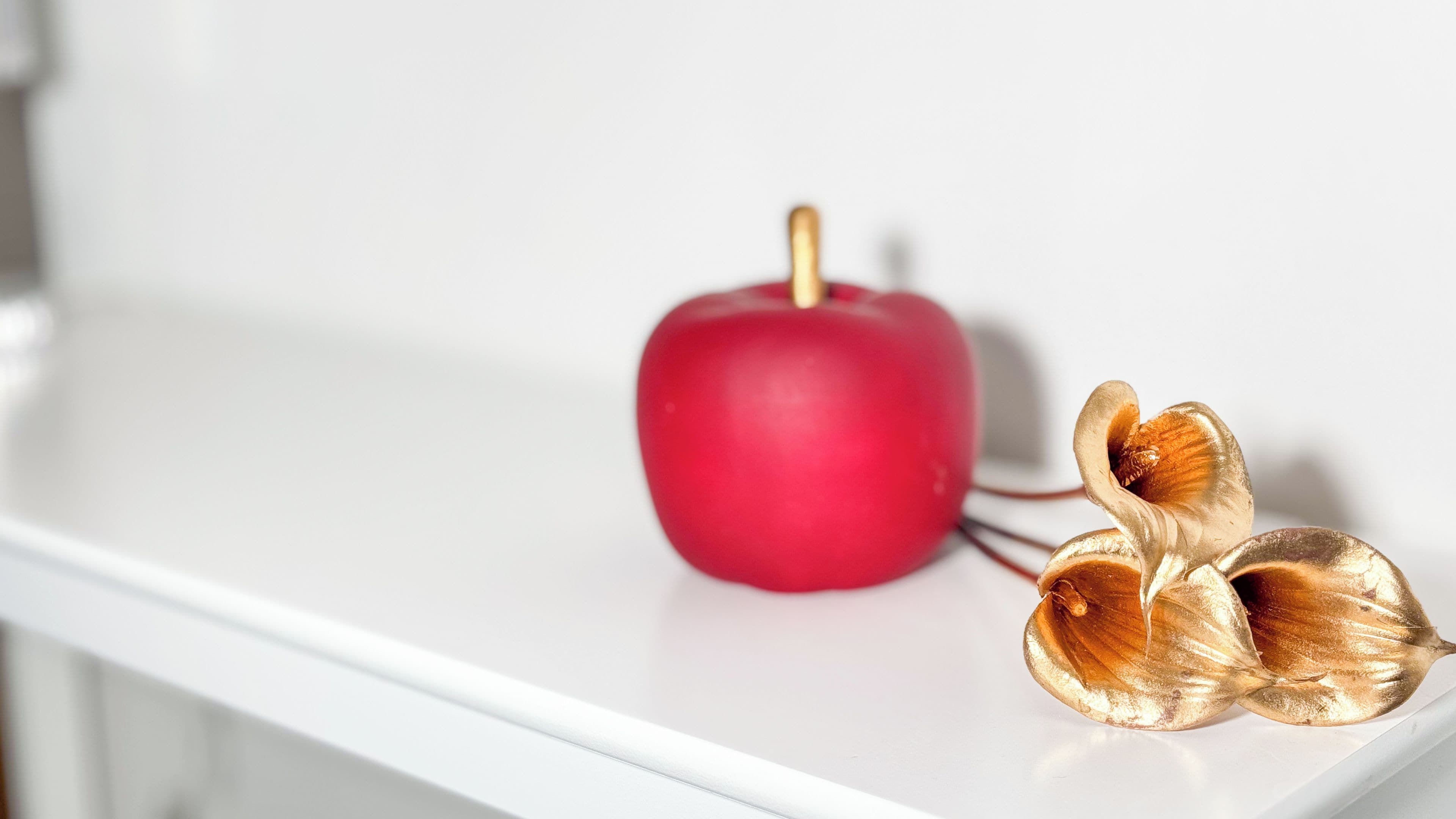 Una manzana roja y dos hojas doradas sobre una superficie blanca.