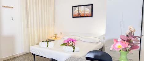 A hotel room with a bed, a bedside table with a lamp, a framed picture on the wall, a wardrobe, and a vase with flowers.