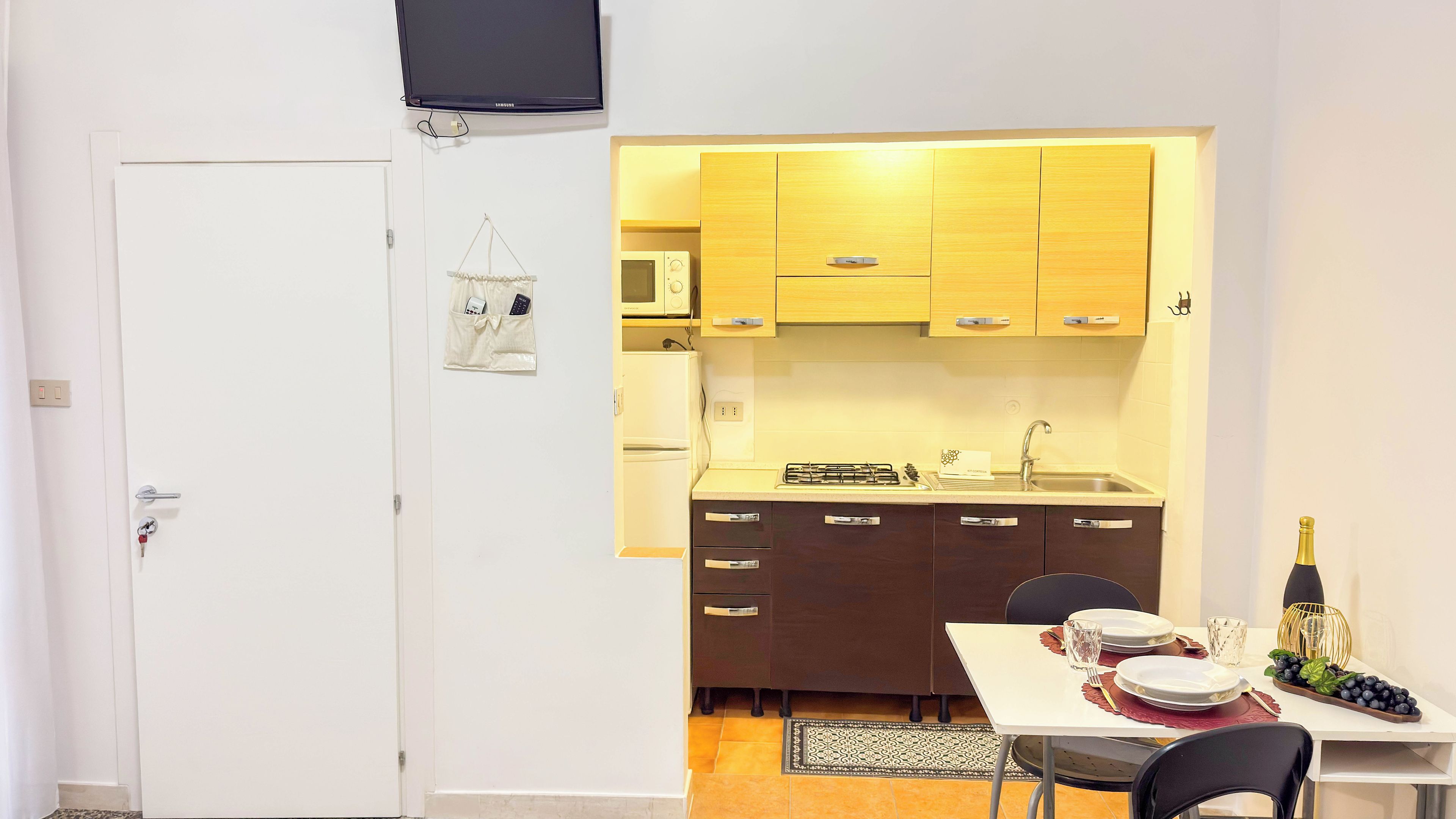 Une cuisine compacte avec des meubles en bois, un four à micro-ondes et une cuisinière à gaz. On y trouve un coin repas avec une table dressée pour deux personnes, une bouteille de champagne et un assortiment de fruits.