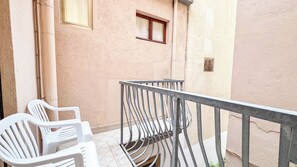 Un balcó amb barana metàl·lica, dues cadires de plàstic blanc i una finestra amb vidre mat.