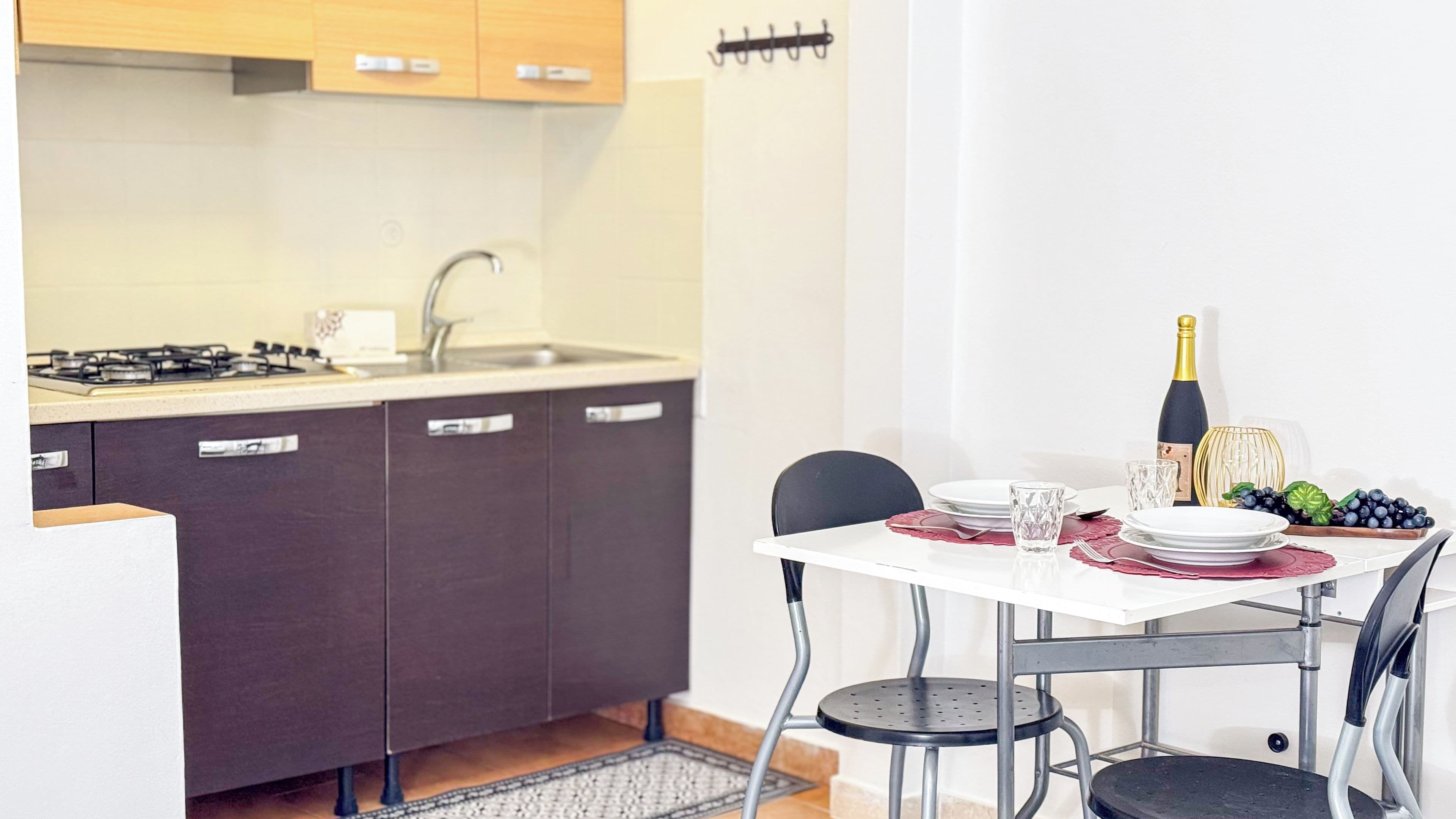 A compact kitchen with a gas stove, dark cabinets, and a white dining table set with plates, glasses, and a bottle of champagne.