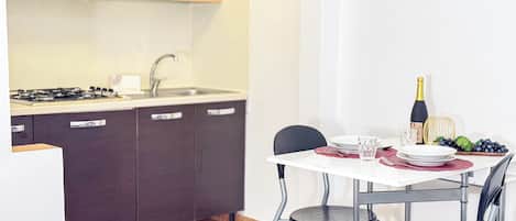 A compact kitchen with a gas stove, dark cabinets, and a white dining table set with plates, glasses, and a bottle of champagne.