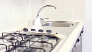 A kitchen with a gas stove, a stainless steel sink, and white tiled walls. - Cà 4 Nevodi Jennifer by Ca-Sa Check - MS 2 NTCà 4 Nevodi Jennifer by Ca-Sa Check - MS 2 NT (Chioggia)