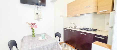 A compact kitchen with a flat-screen TV, wooden cabinets, a gas stove, and a dining table with chairs.