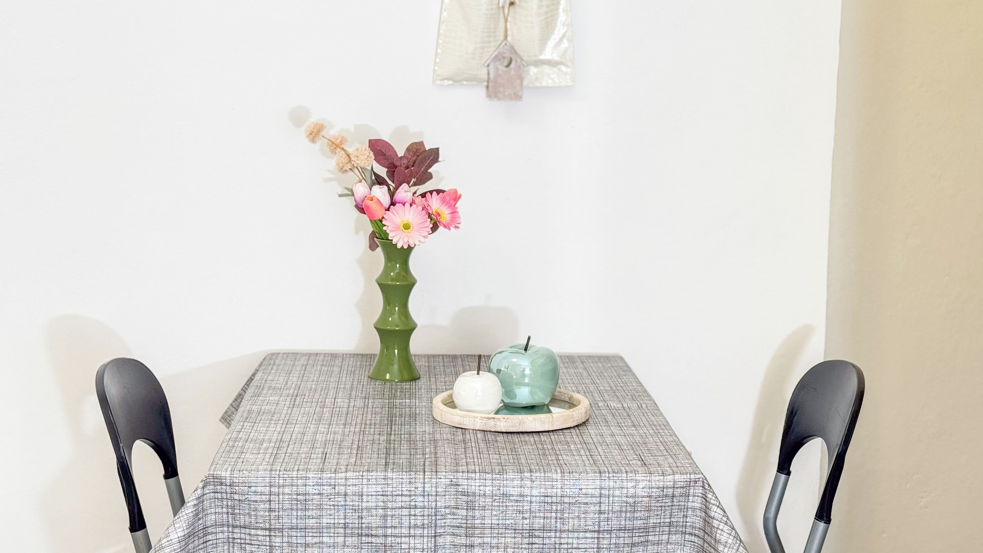 A table with a checkered tablecloth, a green vase with flowers, and a teal teapot on a tray.