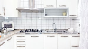 A modern kitchen with white cabinets, a gas stove, a stainless steel sink, and a microwave. - Cà 4 nevodi Chiara by Ca-Sa Check (Chioggia)