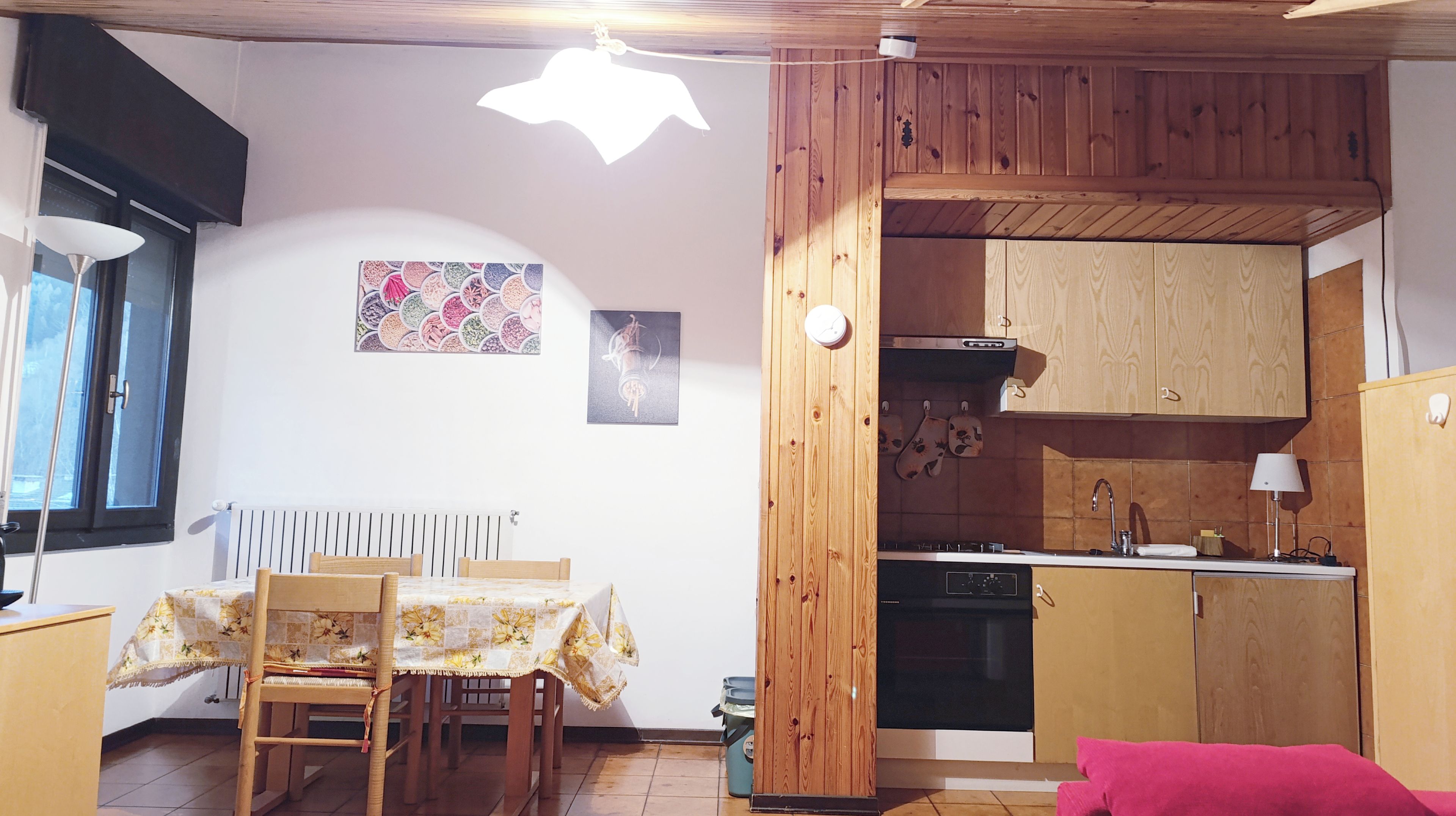 A compact kitchen with wooden cabinets, a built-in oven, and a sink. There is a dining table with chairs and a window with blinds.