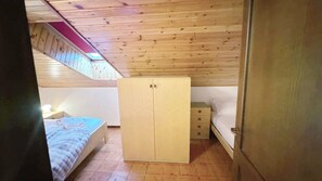 A bedroom with a wooden ceiling, a bed with a blue blanket, a wardrobe, and a small bedside table. - Baradello Apartment & Flat by ca-Sa Check  (Corteno Golgi)