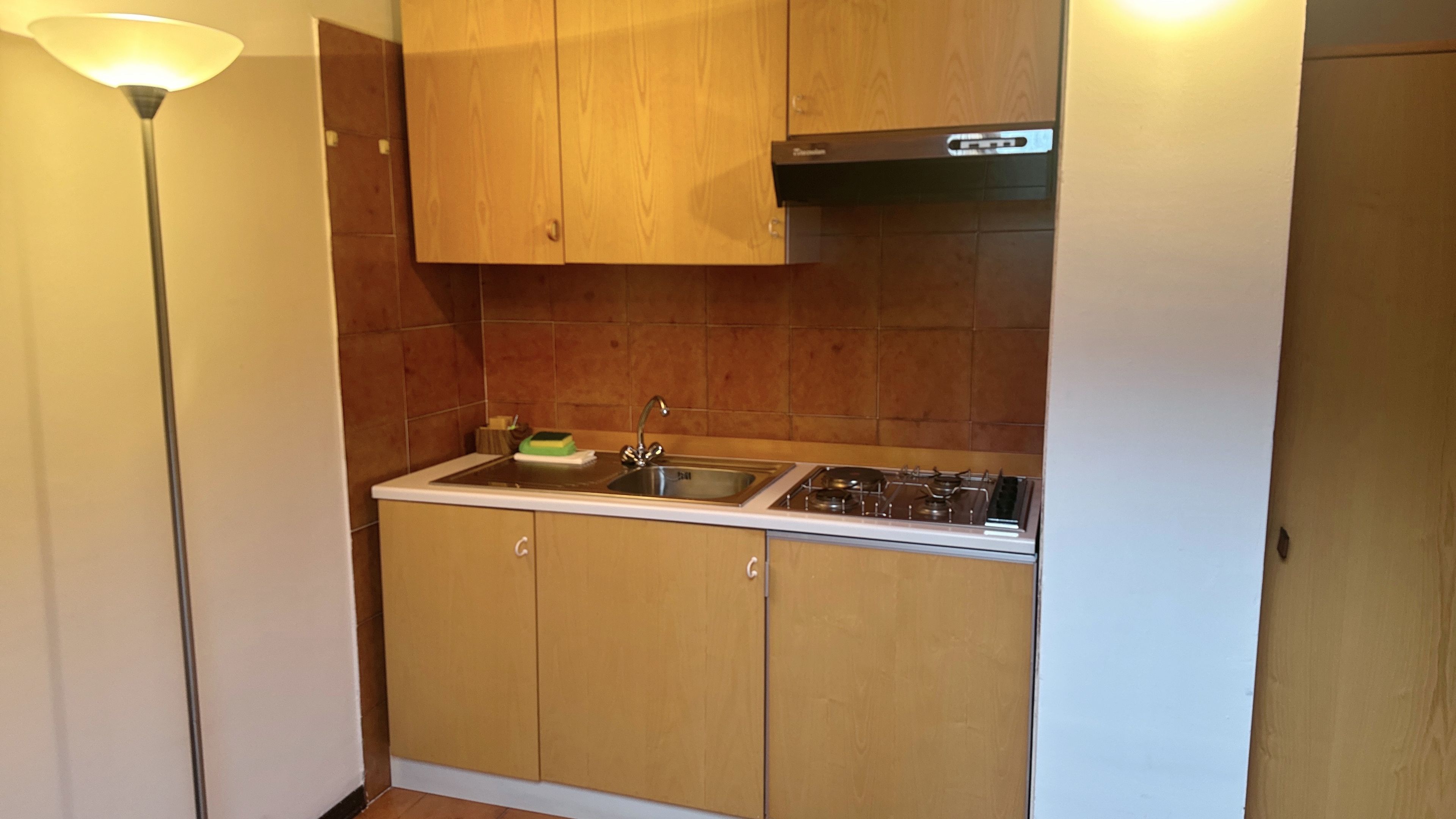 A compact kitchen with wooden cabinets, a stainless steel sink, and a gas stove.