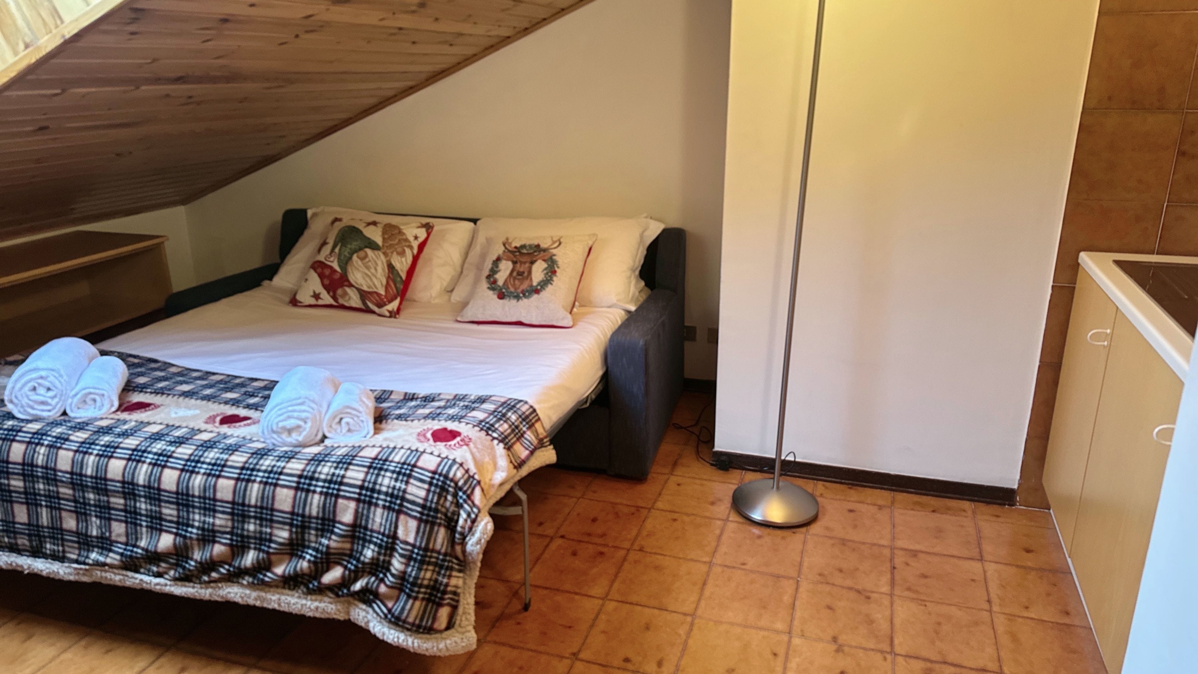 A bedroom with a bed, pillows, a blanket, and rolled towels.