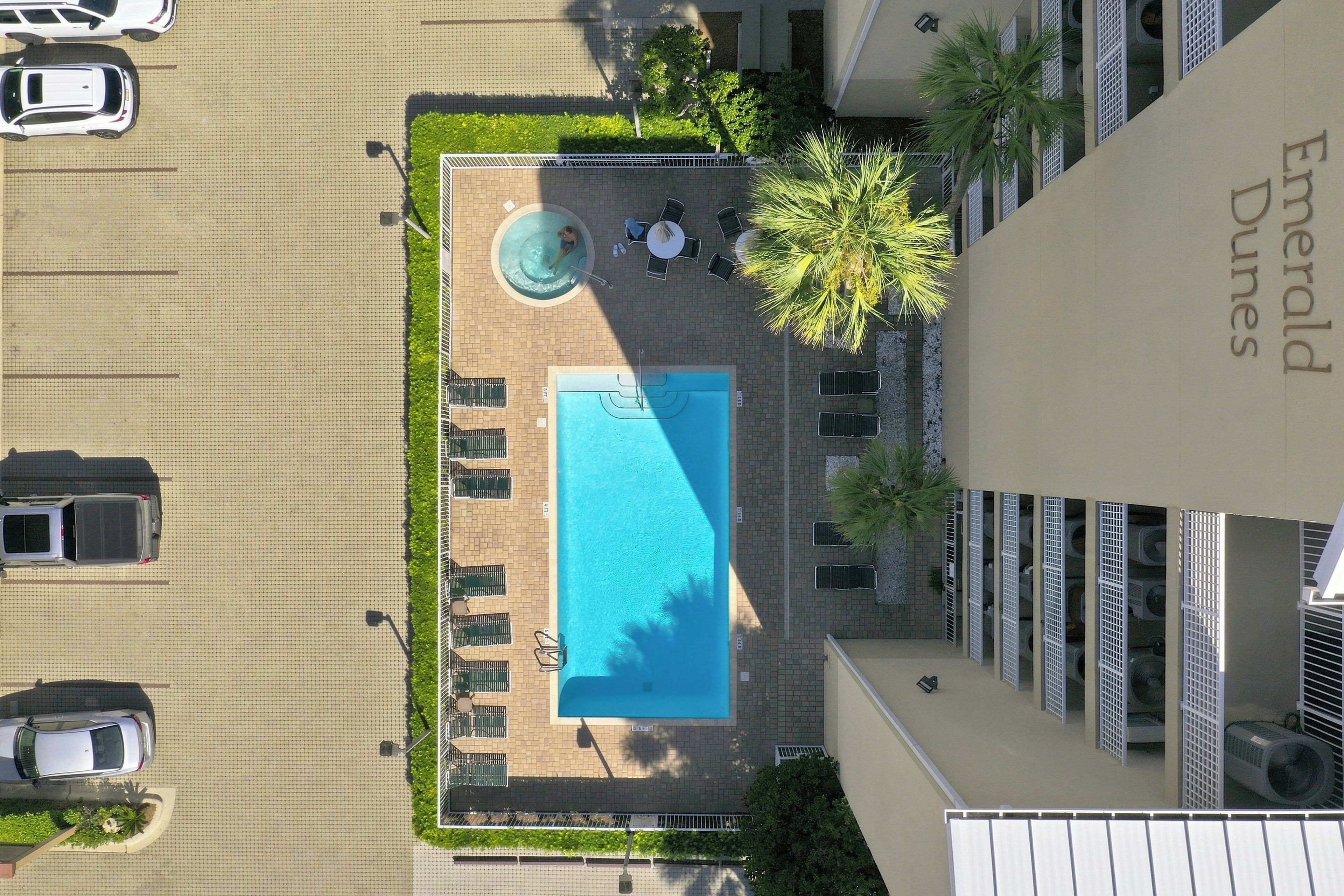 An aerial view of a hotel with a swimming pool, lounge chairs, and a palm tree.