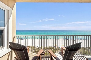 A balcony with two chairs and a table, overlooking a beach with umbrellas and people. - Beachfront Condo with Stunning Gulf Views!  Gated, Balcony, Pool and Hot Tub! (Destin)