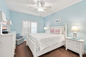 A bedroom with a white bed, a nightstand with a lamp, a dresser, a window with blinds, and a ceiling fan. - Beachfront Condo with Stunning Gulf Views!  Gated, Balcony, Pool and Hot Tub! (Destin)