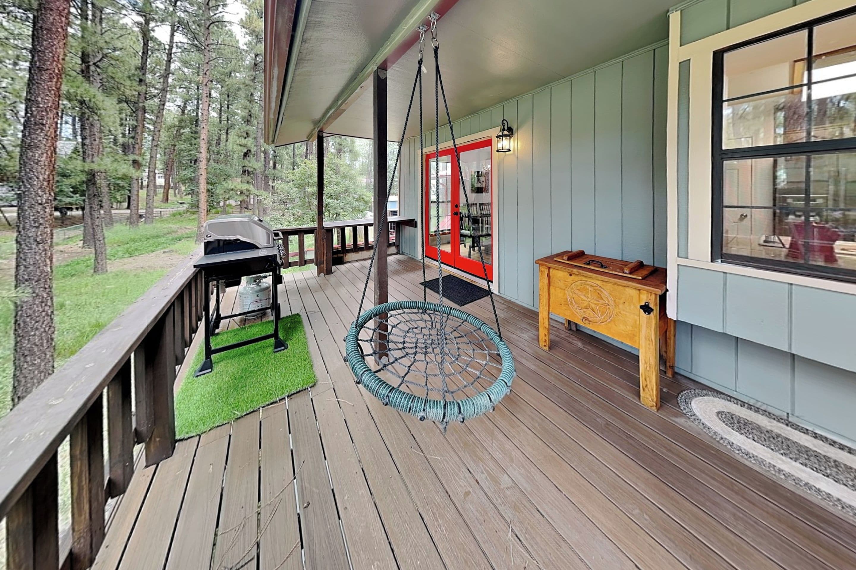 Une terrasse en bois avec un fauteuil suspendu, un barbecue et une table agrémentée d’une lanterne.