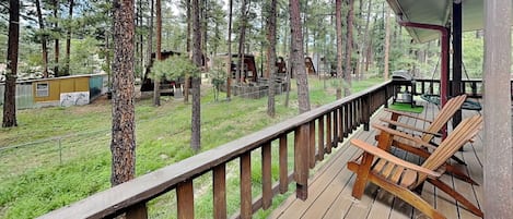 A wooden deck with outdoor seating, surrounded by tall trees.