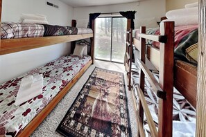 Ein schmales Zimmer mit Etagenbetten, einem Fenster mit Vorhängen und einem gemusterten Teppich.