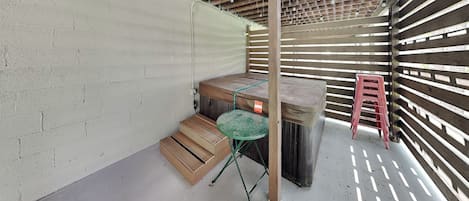 Un espacio al aire libre techado con un banco de madera, una mesa pequeña y un taburete rojo.