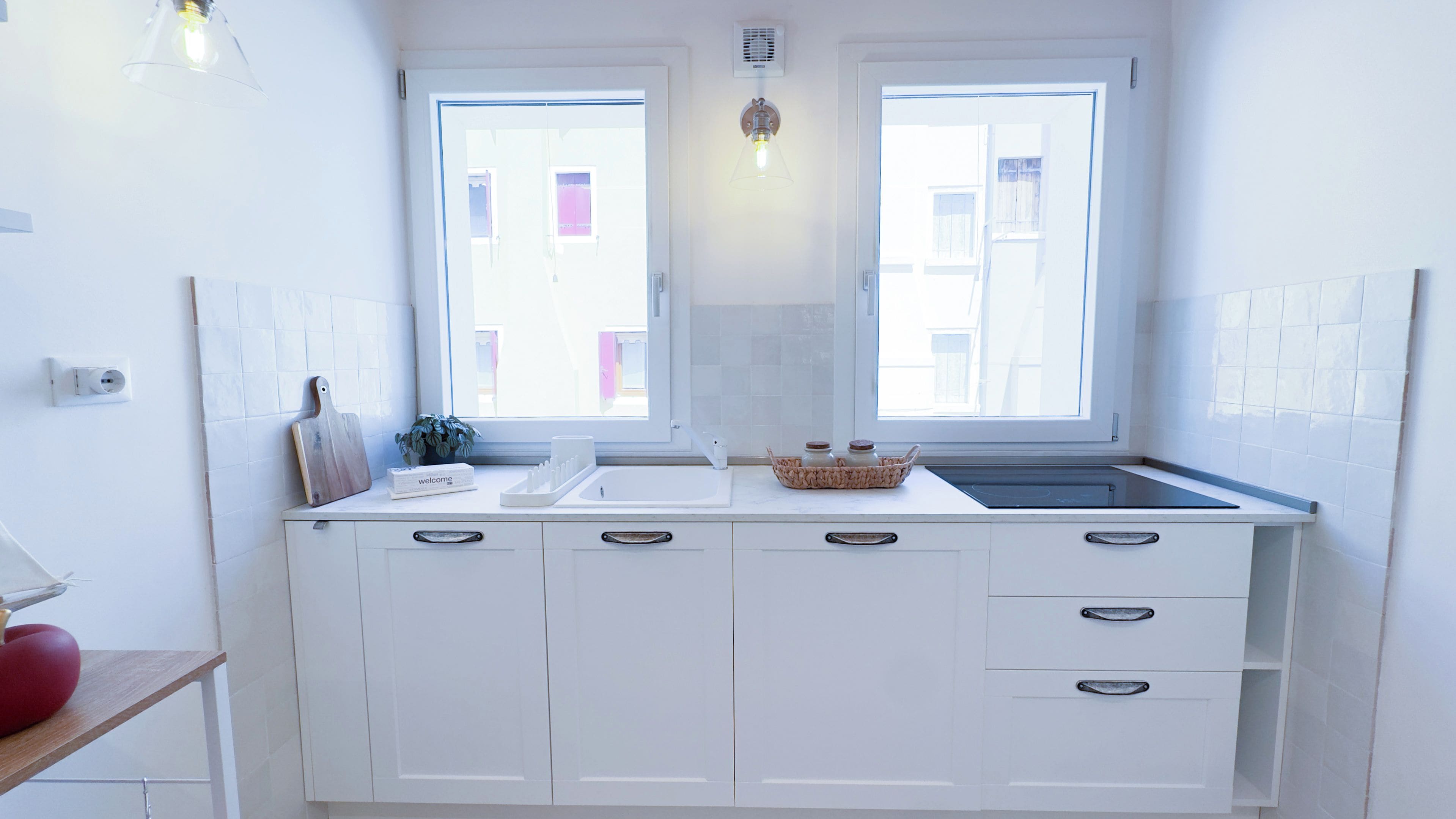 A modern kitchen with white cabinetry, a built-in sink, and two windows.