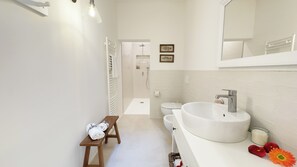 Ein modernes Badezimmer mit einem großen, weißen Waschbecken, einer Duschkabine und einer kleinen Holzbank mit Handtüchern.