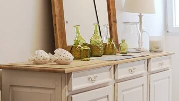 Un mueble blanco de madera con un espejo, botellas de vidrio verde y una lámpara.