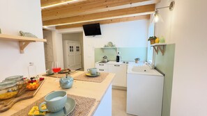 A modern kitchen with white cabinets, a built-in stove, and a sink. There is a wooden ceiling with exposed beams, and a flat-screen TV mounted above the stove.