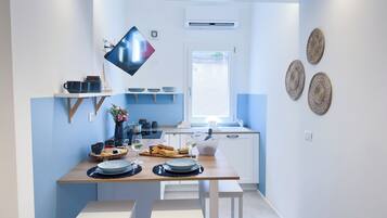 A modern kitchen with a dining table set for two, a TV mounted on the wall, and decorative woven wall art.