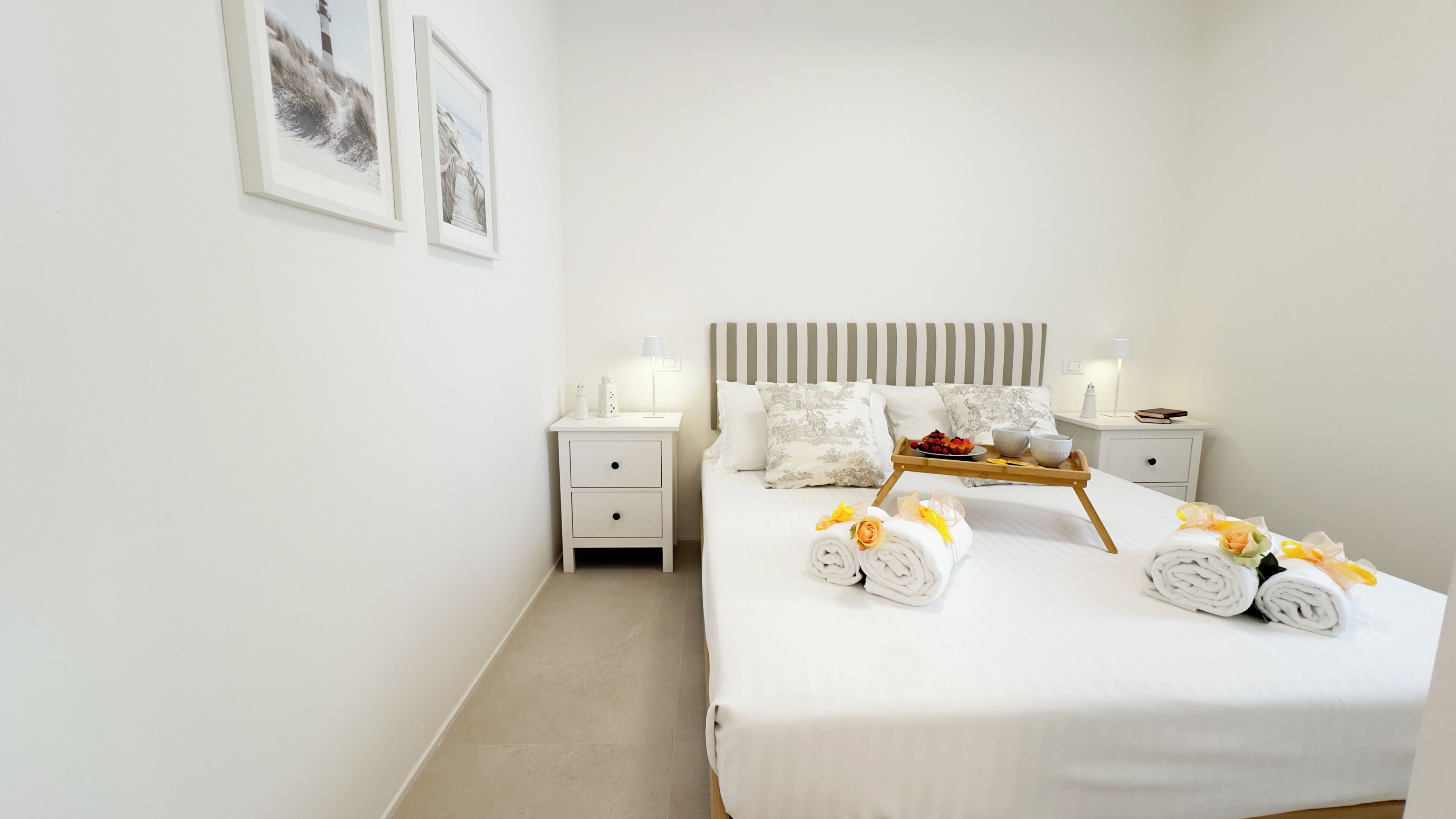 Quarto de hotel bem arrumado, com uma cama grande, duas mesas de cabeceira e cabeceira com listras verticais.