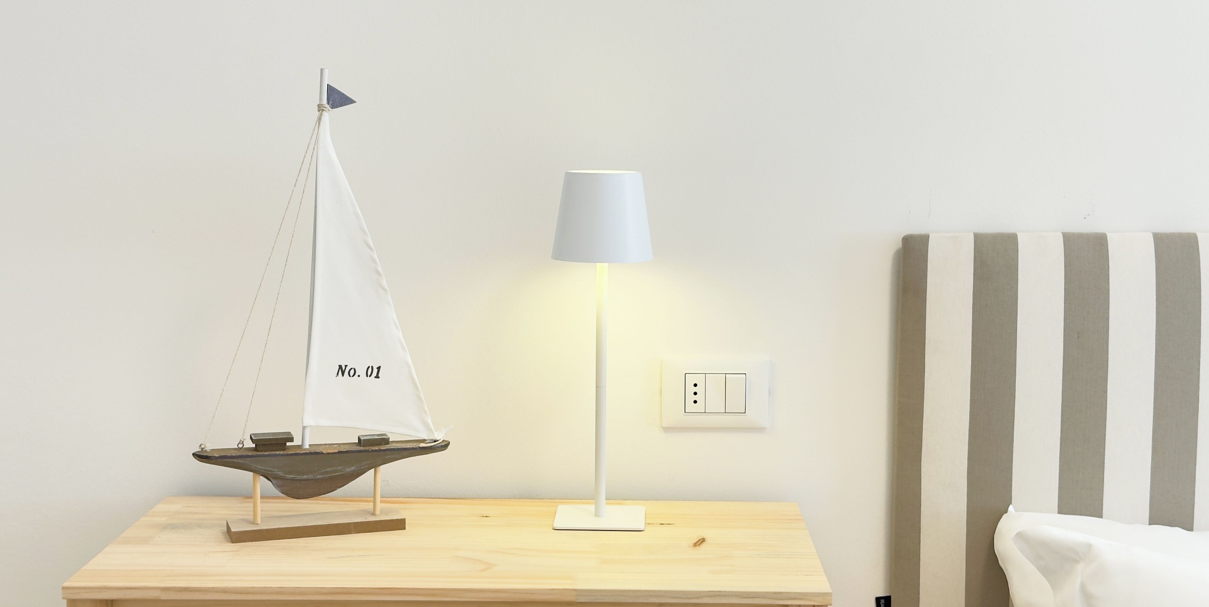 Una mesita de noche de madera con un modelo de velero y una lámpara.