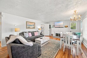 A living room with a grey sofa, a coffee table, and a dining area with a white table and chairs. - Coastal Cottage Near Yaquina Views, Sleeps 6 (Newport)