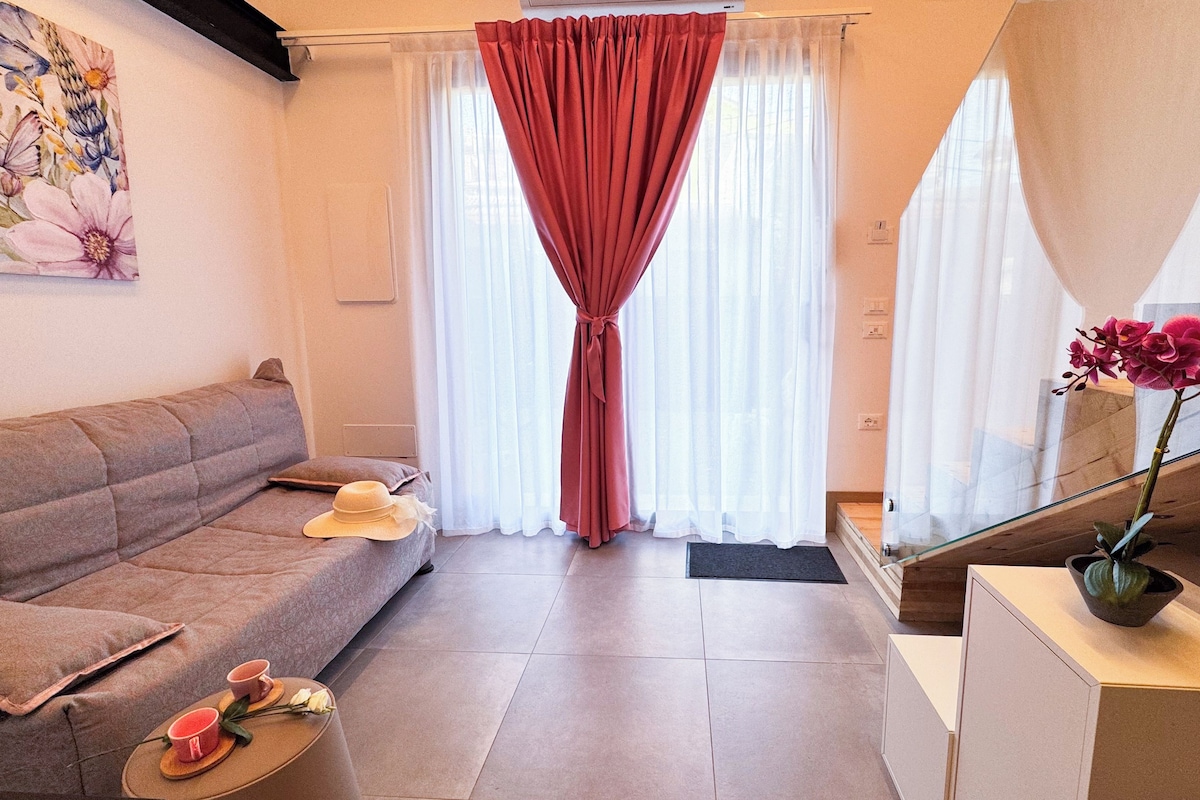 Uma sala de estar moderna com um sofá, uma mesa de centro com uma xícara e um chapéu, uma escada e uma orquídea em vaso.