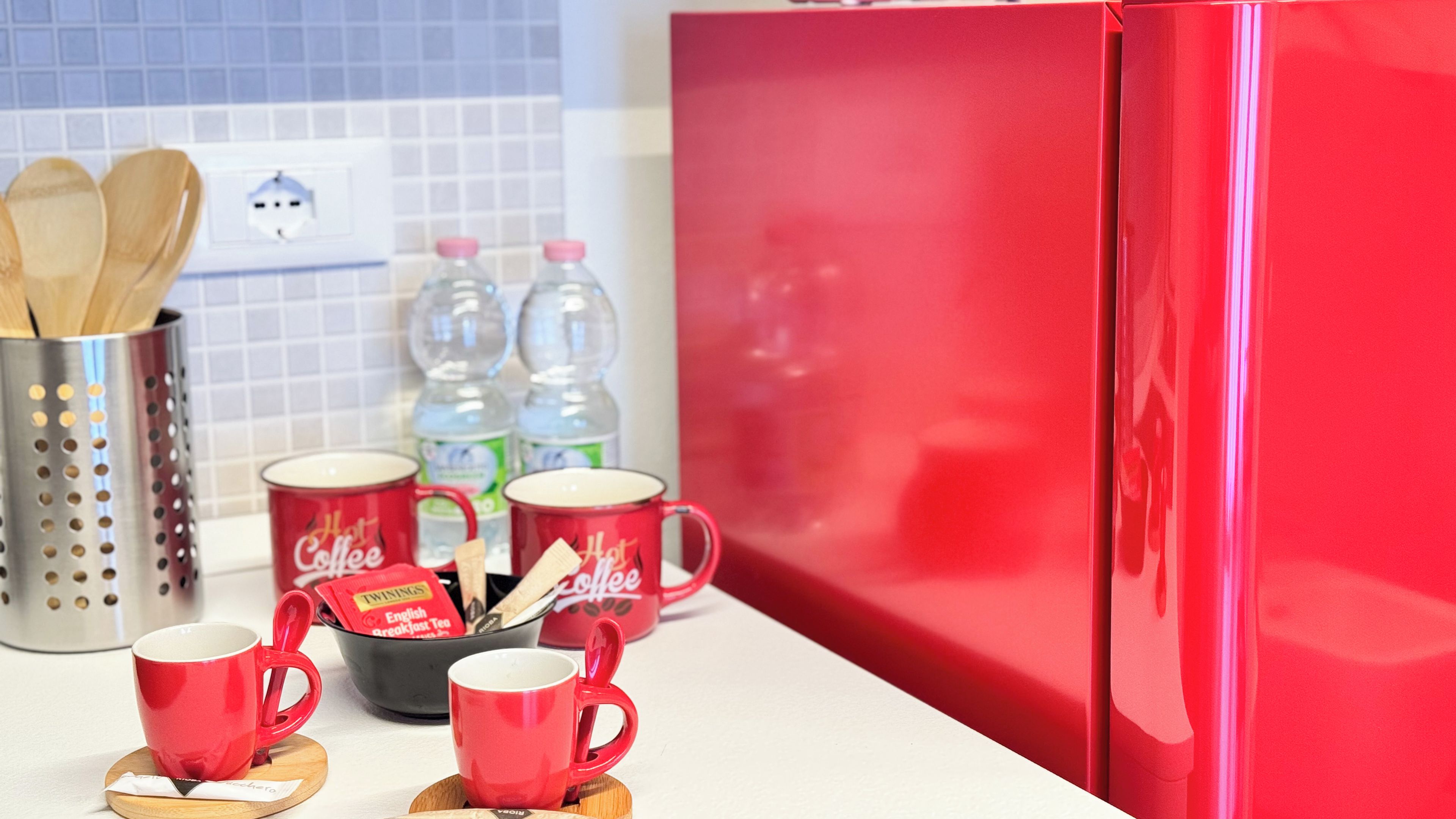 Uma bancada de cozinha com canecas vermelhas, uma cafeteira e uma geladeira vermelha.