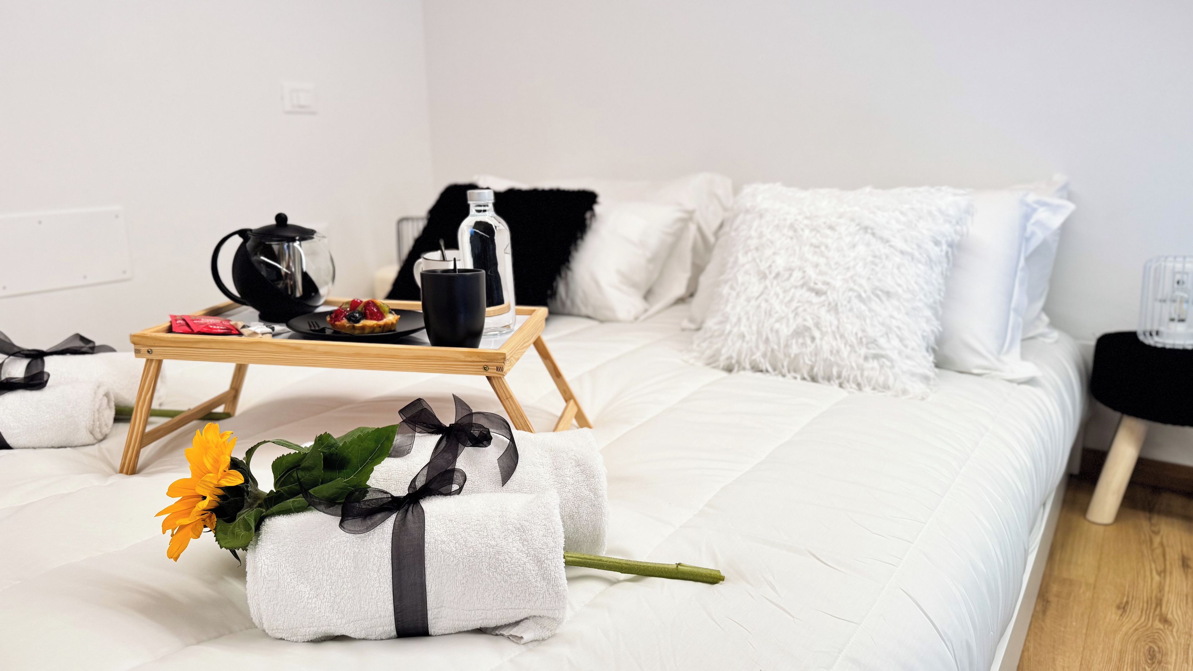 Un lit bien fait, avec du linge de lit blanc, un plateau contenant des articles pour le petit-déjeuner et un bouquet de fleurs posé sur le lit.