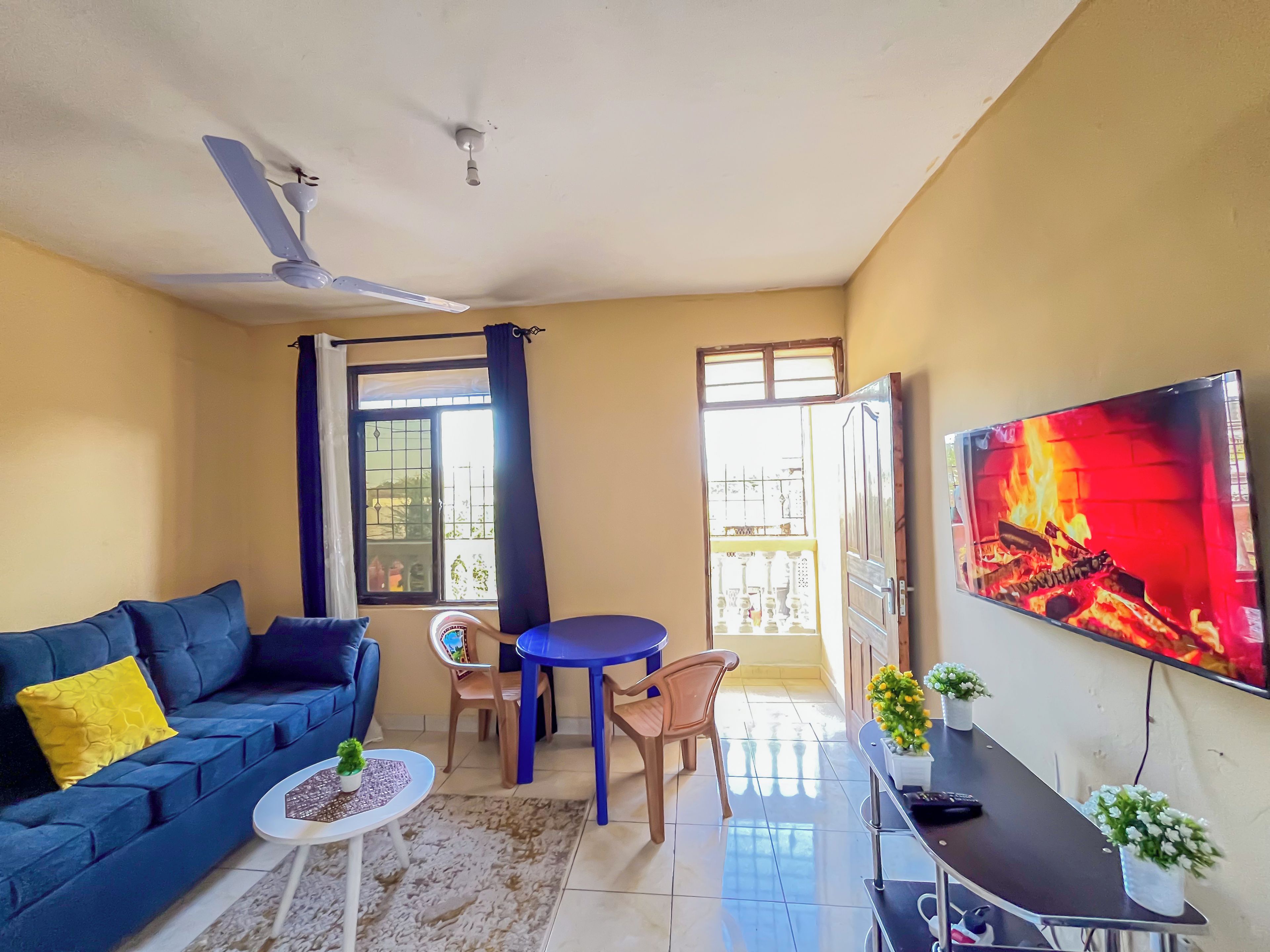 Uma sala de estar com sofá, uma mesinha, televisão e ventilador de teto.