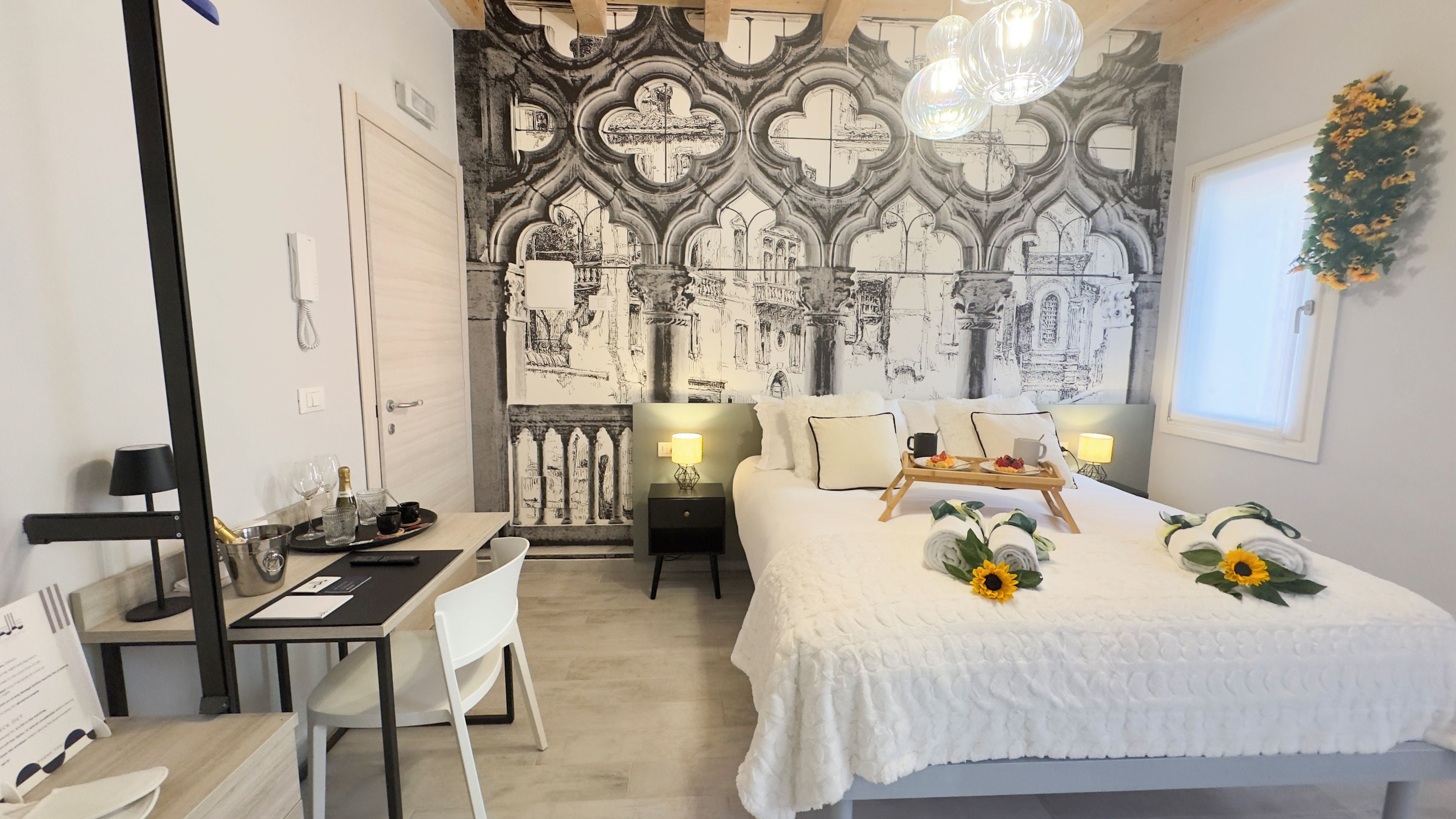 Ett hotellrum med en stor säng, ett skrivbord med en stol, ett litet bord med ett bricka och en vägg prydd med en detaljerad väggmålning.