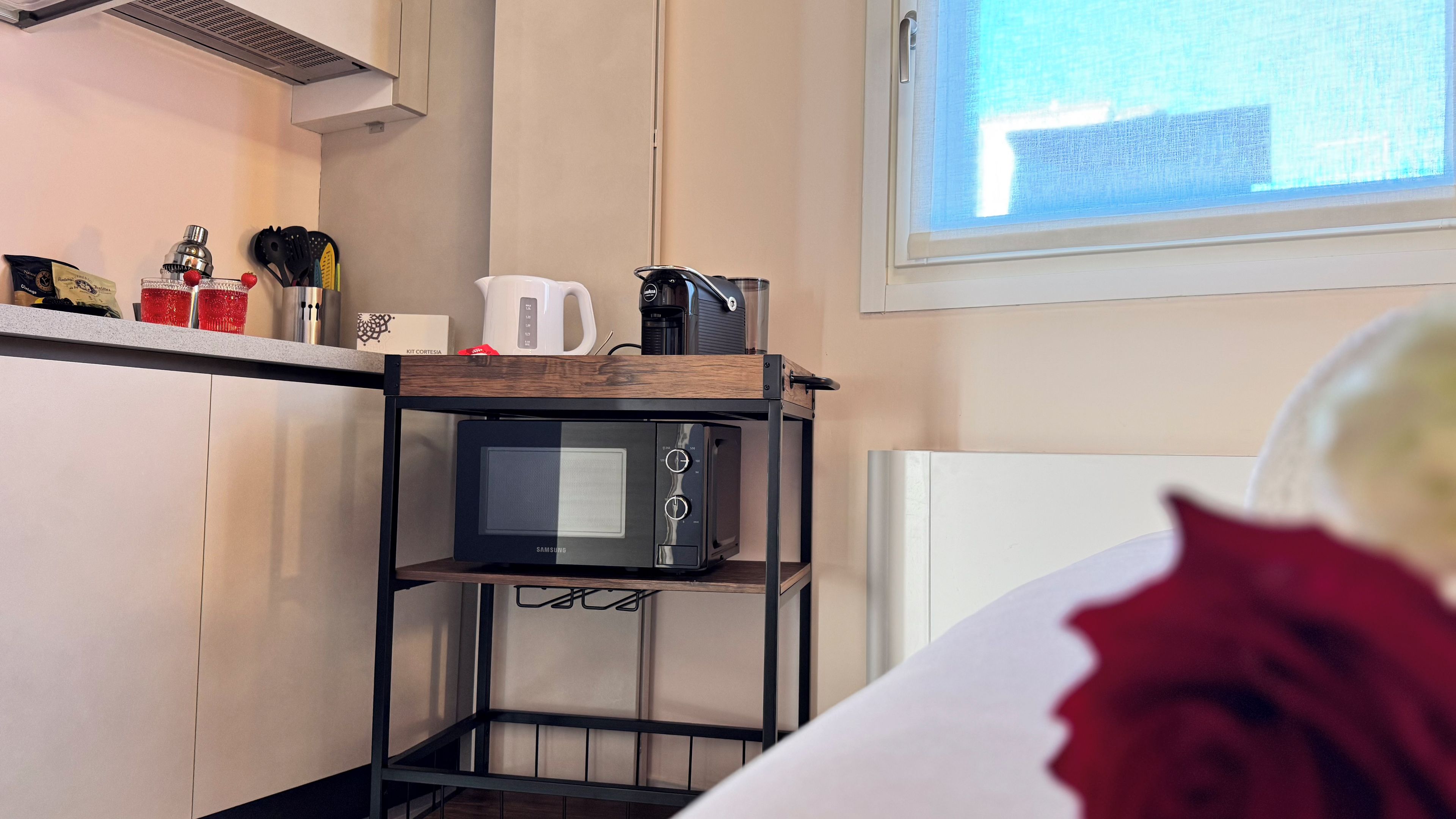 Une cuisine compacte équipée d’un four à micro-ondes, d’une machine à café et d’ustensiles rangés sur une étagère.