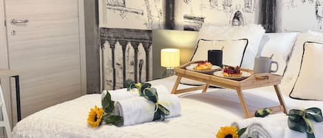 En pænt redt seng med et bakke med morgenmad, en lampe og en væg med et detaljeret muralmaleri.