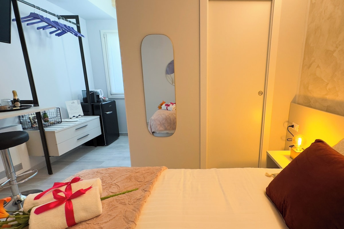 Ein Hotelzimmer mit Bett, Nachttisch, Spiegel und Schreibtisch mit Stuhl.